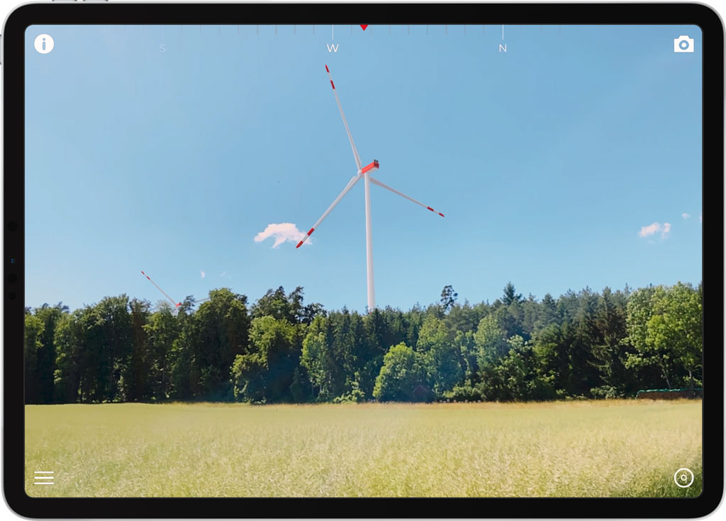 Mockup of an Apple iPad Pro mobile device with live screenshot of WisardGo Augmented Reality App with 2 visualized wind turbines at the edge of the forest